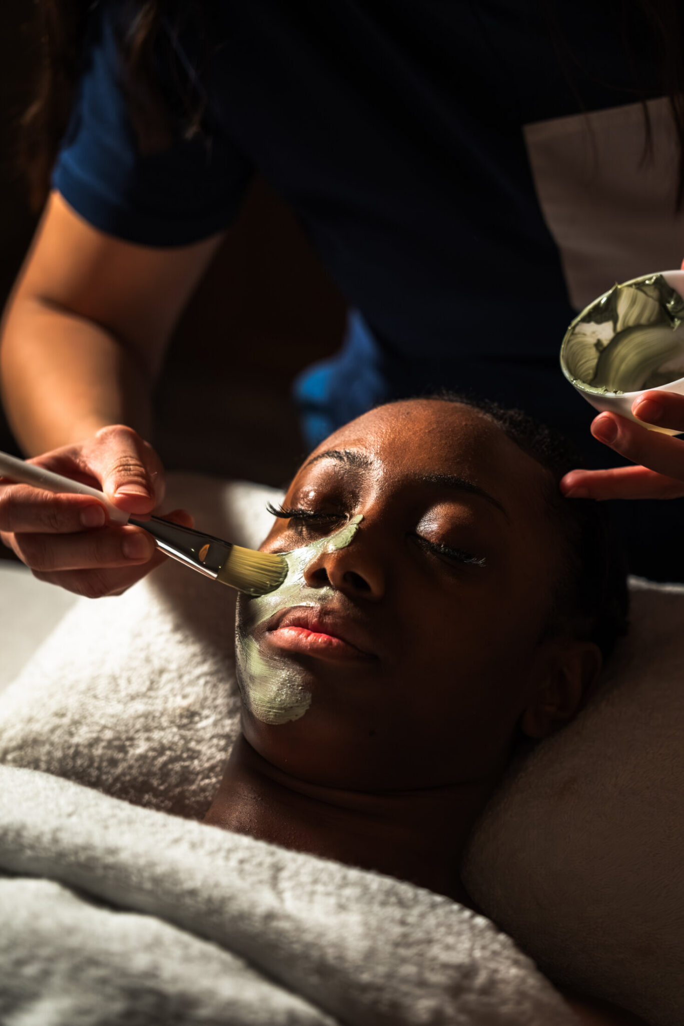 A guest relaxing while one of The Newman spa therapists brushes a green clay mask on their skin during a facial
