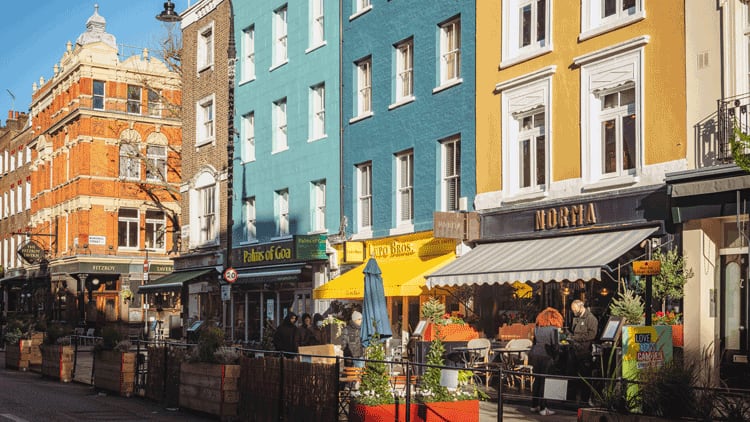 Colourful Georgian townhouses line a sunny Fitzrovia street with alfresco restaurant terraces and diners below.